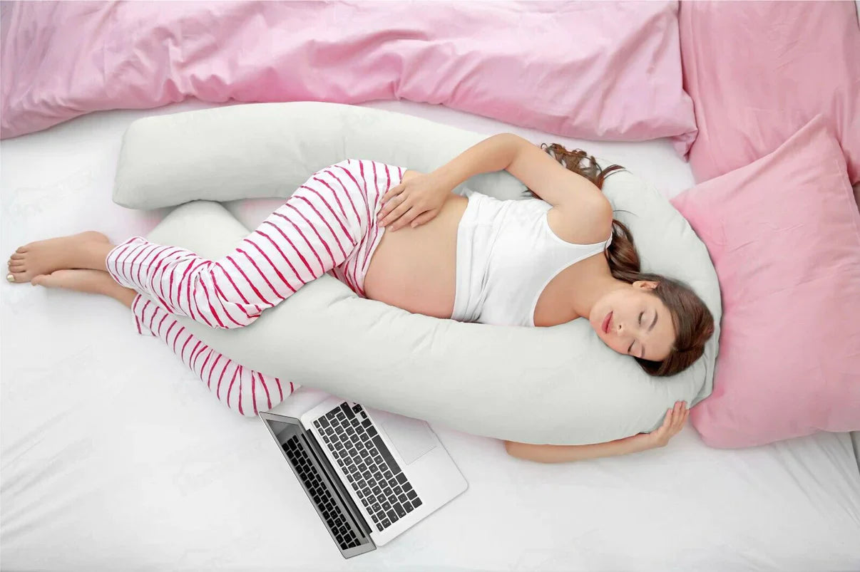 Woman lying on a U-shaped body pillow with a laptop on a bed